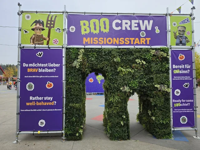 The BOO CREW Missionsstart gate: a tunnel of artificial greenery between purple banners, asking in German and English whether you would rather stay well-behaved or are ready for some BOO-schief