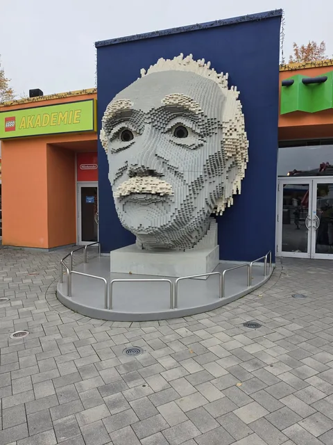 A huge brick-built head of Albert Einstein in grey and white bricks on a plinth in front of the LEGO Akademie building
