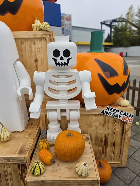 A giant brick-built skeleton minifigure holding a small pumpkin, with a sign reading "Keep calm and say BOO"