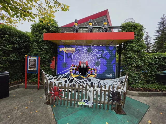 A giant red and black brick-built spider under a canopy in front of a purple Halloween backdrop reading "It's BOO time!"