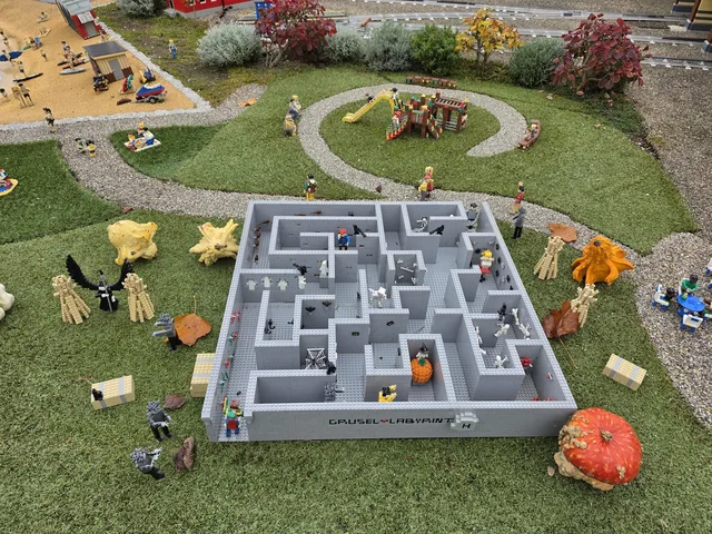 A brick-built miniature maze in Miniland labelled "Grusel-Labyrinth", full of skeletons, ghosts, spider webs and a witch on a pumpkin, with real pumpkins and gourds on the lawn around it