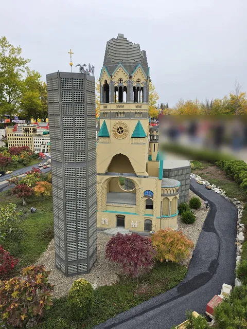 The Kaiser Wilhelm Memorial Church in Miniland: the ruined old tower with its broken spire next to the new octagonal bell tower, surrounded by red and orange shrubs