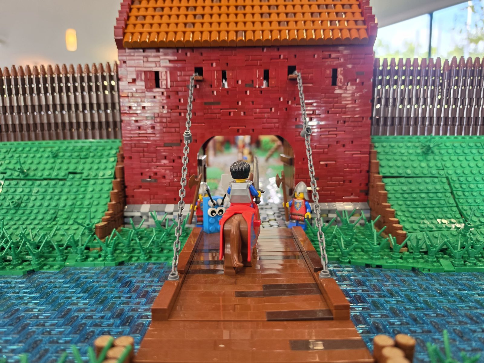 Close-up of a red LEGO castle gate with a wooden drawbridge over a moat