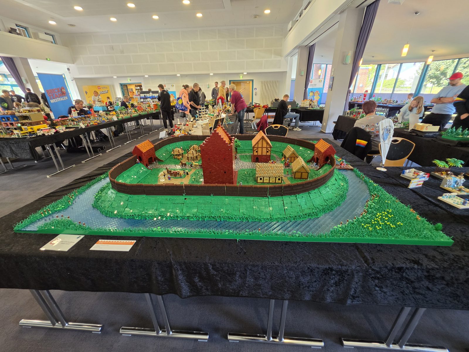 A view across the hall at the Hamme Forum: in the foreground a palisaded village with a moat, behind it the exhibition tables and visitors